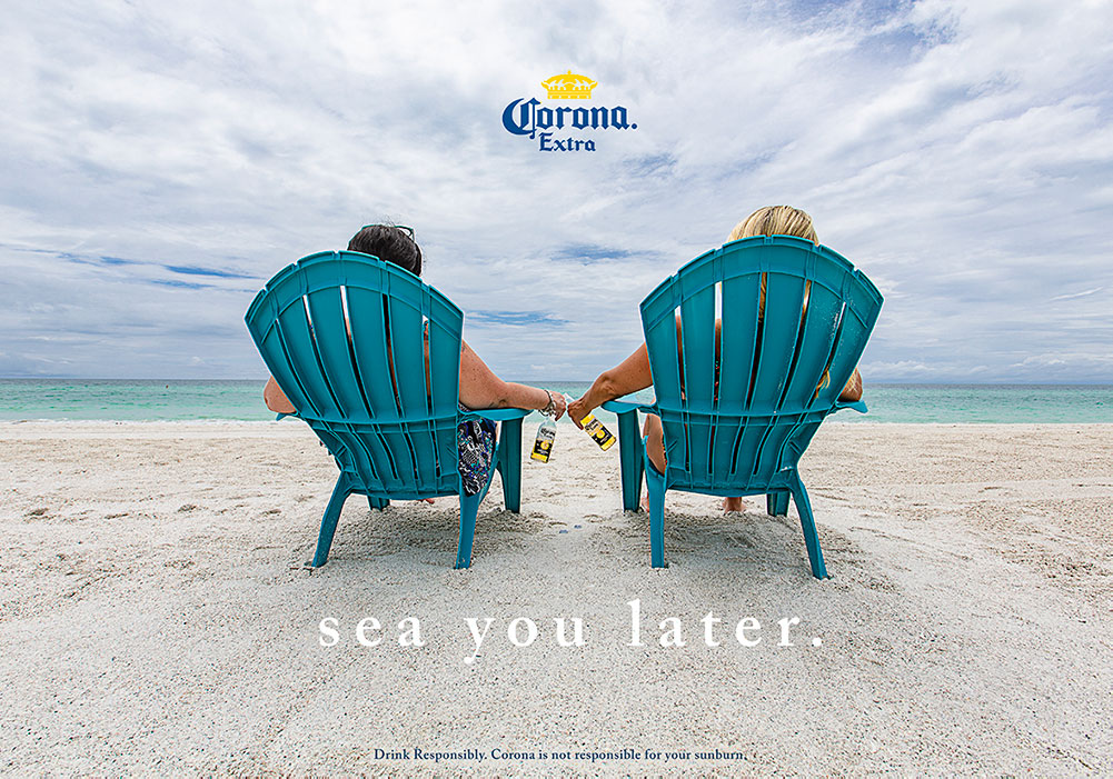 After Photo: of two woman on lawn chairs sitting on the beach holding corona's while looking at the blue ocean. Corona logo and tagline 'sea you later' were added